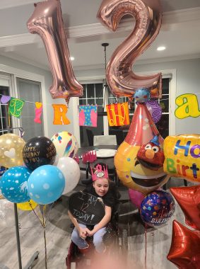 birthday | Rett Syndrome News | a girl at bottom center, with balloons to her left and right, "birthday" spelled out in letters behind her, and two giant balloons reading 12 above her