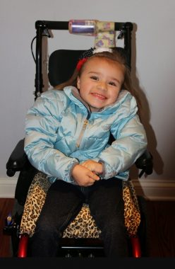 Cammy, who has reddish blond hair and wears a light torquoise jacket, sits in a chair with what appears to be a leopard-print seat. 
