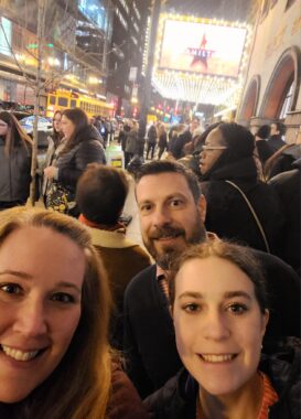 A couple and their daughter take a selfie outside of a theater in Chicago, where "Hamilton" is being performed. They're standing on a crowded sidewalk and the marquee is lit up in the background.