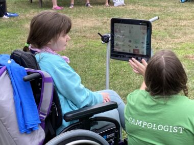 A woman in a wheelchair is helped in the use of an assistive device.